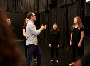 An acting teacher training his students in a room with black cutrains.